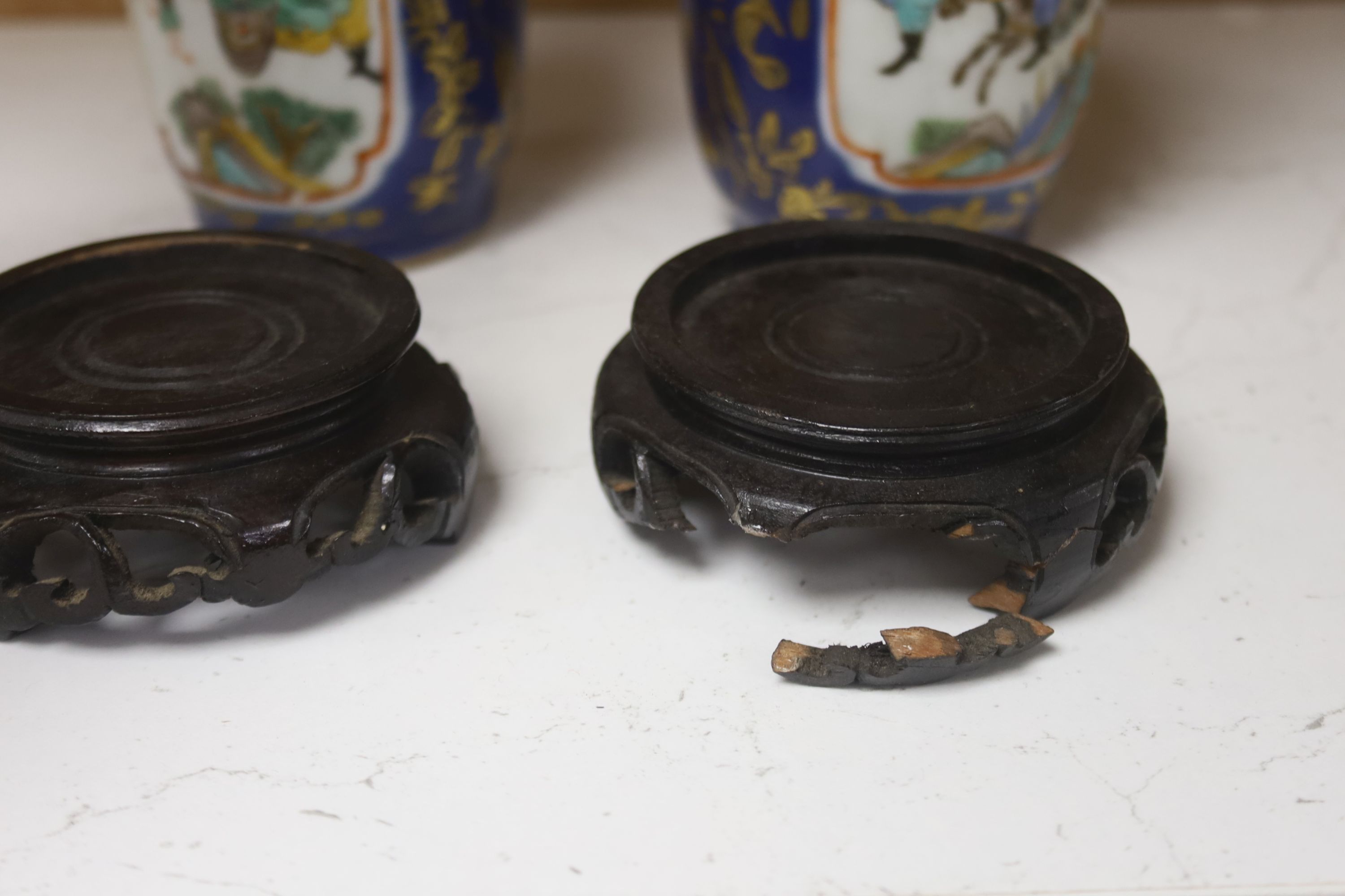 A pair of Chinese Kangxi style blue-ground vases, late 19th century decorated with panels of warriors and heightened in gilt, on carved hardwood stands, height 18cm excluding stand